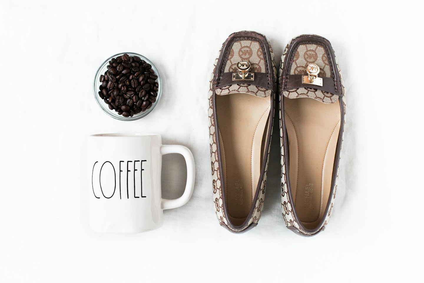Kaffeetasse, Kaffeebohnen und gemusterte Loafer auf weißem Stoff.