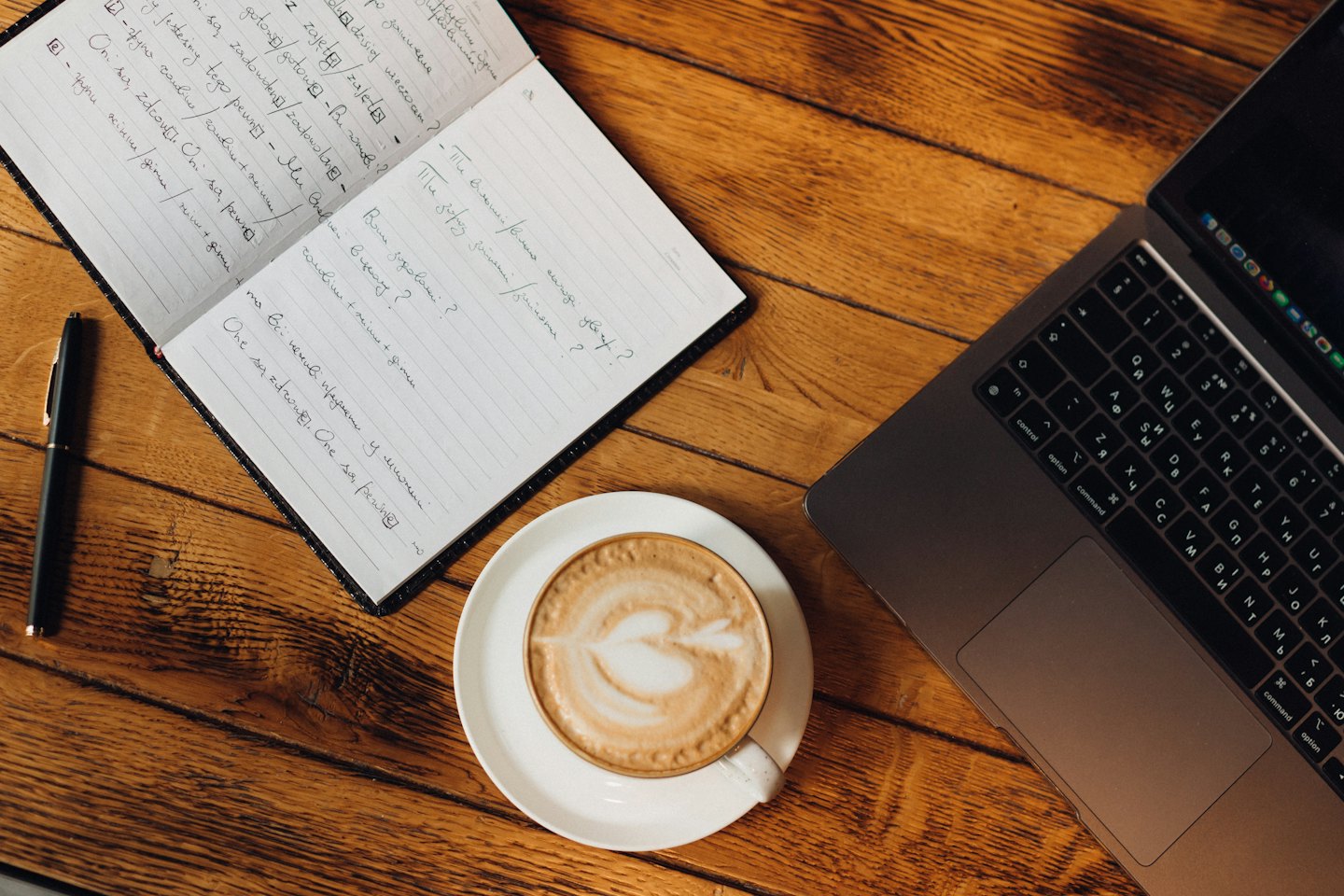 Laptop, Notizbuch und Kaffee auf einem Holztisch.
